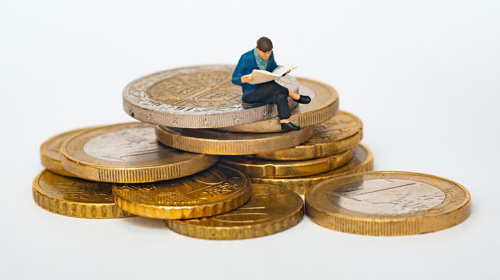 small figurine man reading newspaper on a stack of coins 1